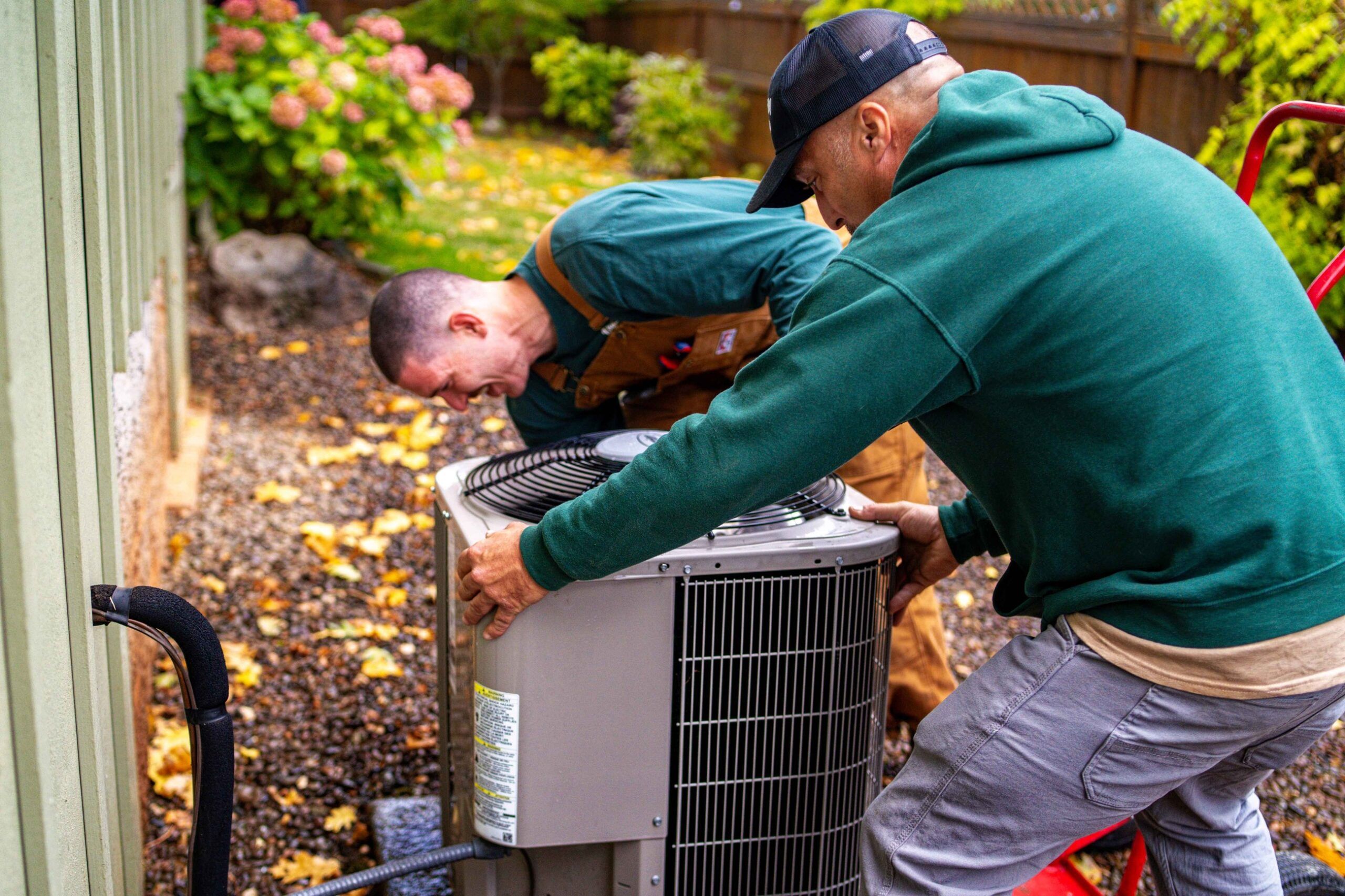 HVAC technicians installing an outdoor air conditioning unit beside a residential house in Grants Pass.