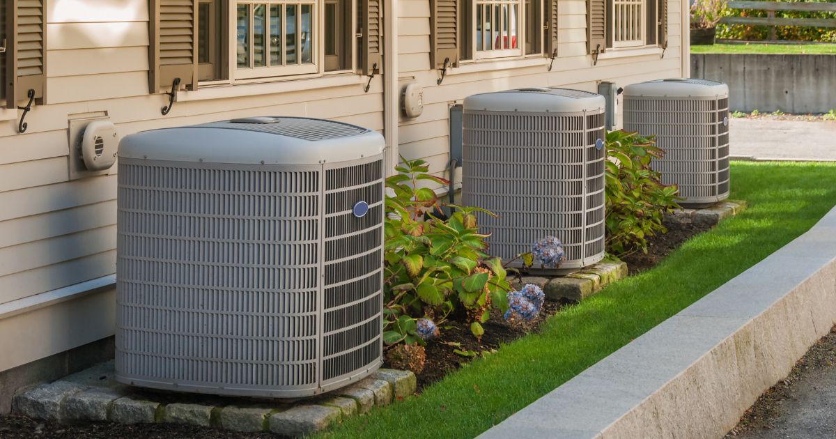 Three large air conditioning units stand on concrete slabs beside a residential house in Grants Pass.